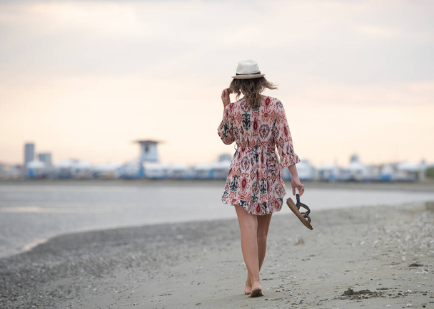 Привлекательная женщина ходит босиком по песчаному пляжу. Туристическая девушка на пляже летом - Фото, изображение