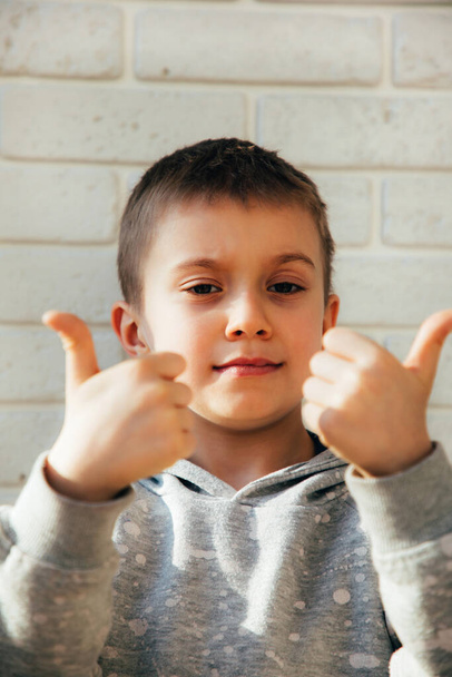 Portrait of a schoolboy against a white brick wall with thumbs up - Foto, afbeelding