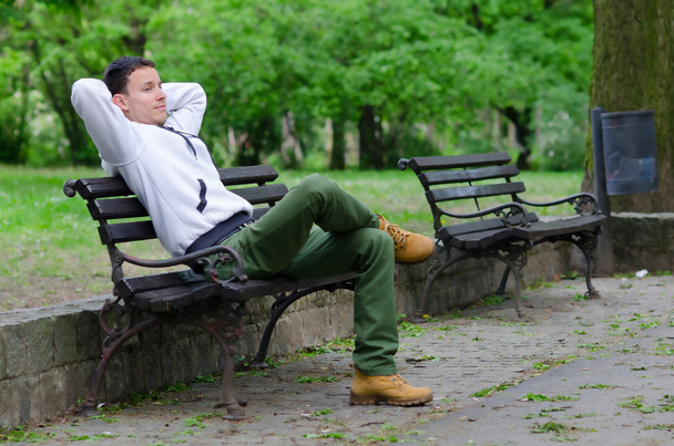 jonge man zittend op de bank in het park - Foto, afbeelding