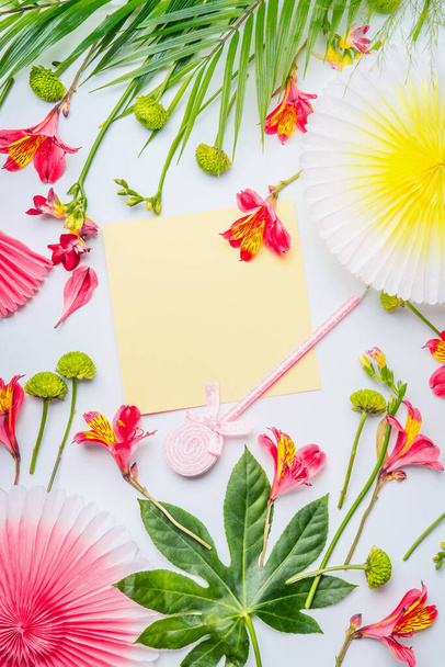 Yellow greeting card mock up with paper party fans, tropical leaves and flowers on white background, top view. Vertical. Flat lay. Frame. Copy space for your text or design - Photo, Image