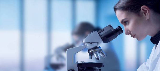 Young researcher working in the lab, she is looking through a microscope and checking samples, medical research concept - Foto, Imagem