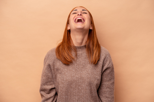 Νεαρή καυκάσια γυναίκα απομονωμένη σε μπεζ φόντο χαλαρό και χαρούμενο γέλιο, λαιμός τεντωμένος που δείχνει τα δόντια. - Φωτογραφία, εικόνα