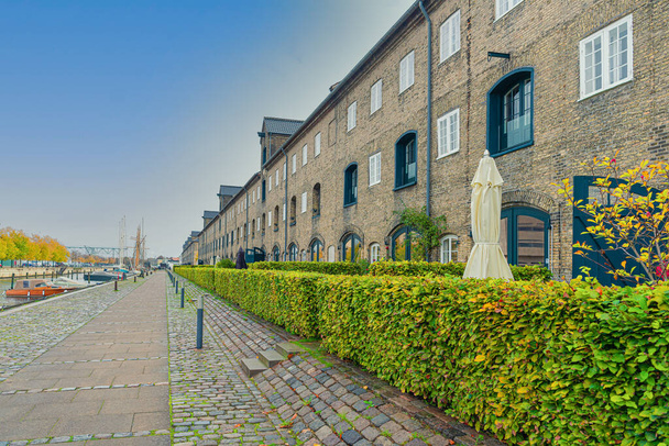 Viele dreistöckige Gebäude aus grauen Ziegeln an einer Straße mit Steinpflaster in der Nähe des Flusskanals im Stadtteil Christianshavn.Kopenhagen, Dänemark - Foto, Bild