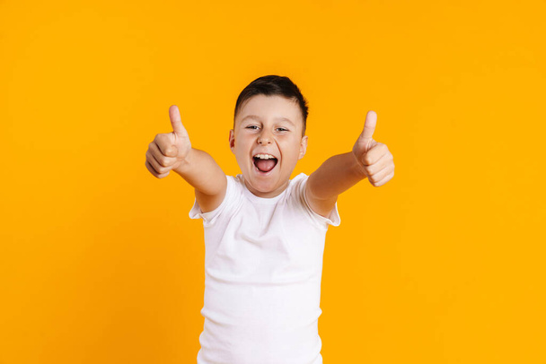 Happy smiling preteen boy in t-shirt standing over yellow background giving thumbs up - Valokuva, kuva