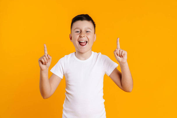Happy smiling preteen boy in t-shirt standing over yellow background presenting copy space - Fotoğraf, Görsel
