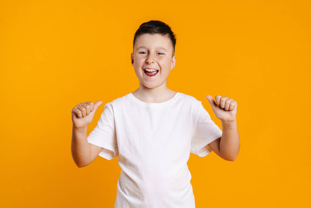 Happy smiling preteen boy in t-shirt standing over yellow background pointing fingers at himself - Φωτογραφία, εικόνα