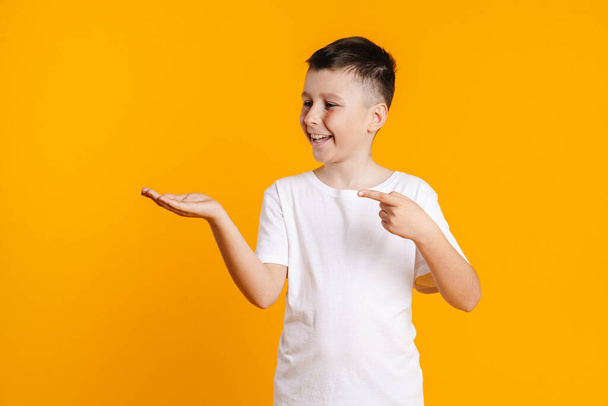Happy smiling preteen boy in t-shirt standing over yellow background presenting copy space - Foto, imagen