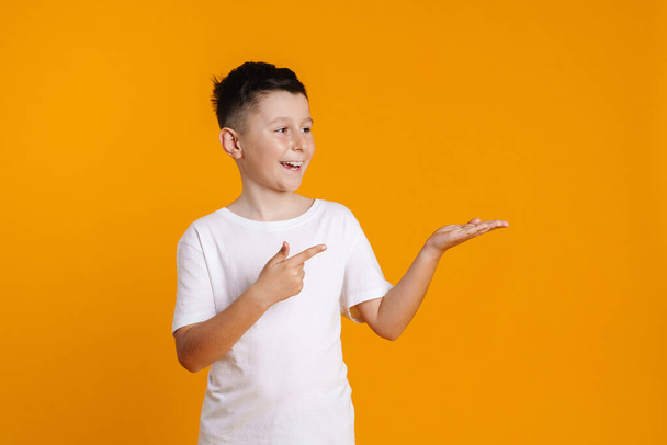Glücklich lächelnder Frühchen-Junge im T-Shirt, der vor gelbem Hintergrund steht und Kopierraum präsentiert - Foto, Bild