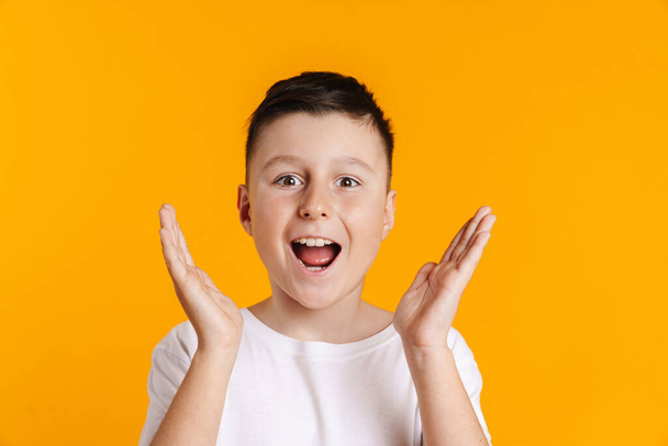 Happy smiling excited preteen boy in t-shirt standing over yellow background holding arms at face - Foto, Bild