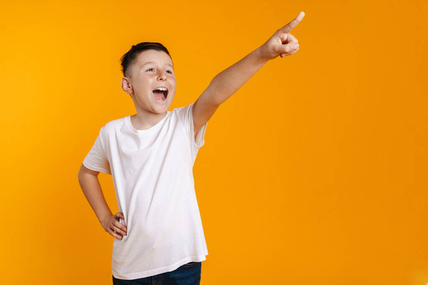 Happy smiling preteen boy in t-shirt standing over yellow background presenting copy space - 写真・画像