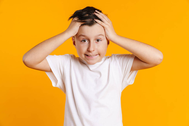 Confused preteen boy in t-shirt standing over yellow background gesturing - Foto, Imagem