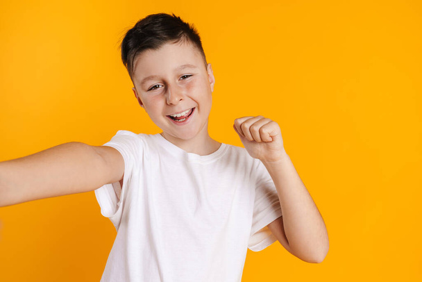 Brunette white boy taking selfie photo and making winner gesture isolated over yellow background - Foto, imagen