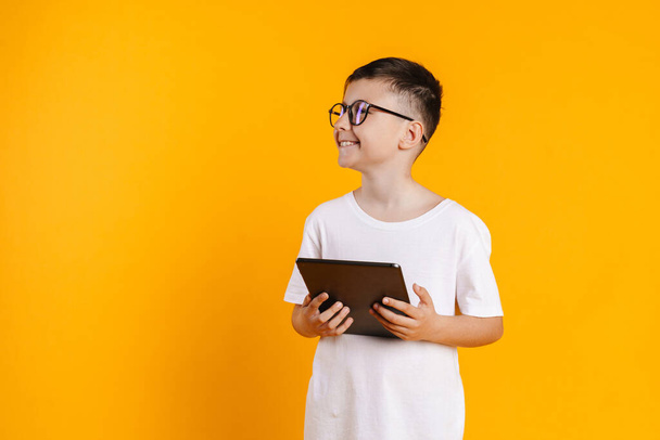Happy smiling preteen boy in t-shirt standing over yellow background holding digital tablet computer - Zdjęcie, obraz