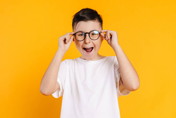 Happy smiling preteen boy in t-shirt standing over yellow background wearing glasses - Fotó, kép