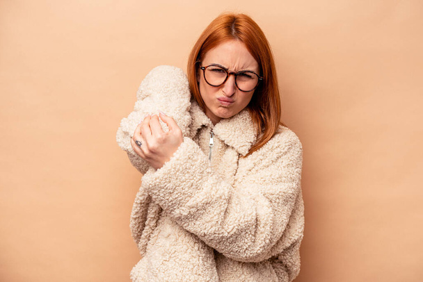 Jeune femme caucasienne isolée sur fond beige ayant une douleur au cou due au stress, le massant et le touchant à la main. - Photo, image