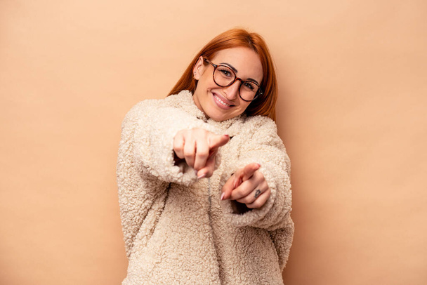 Young caucasian woman isolated on beige background pointing to front with fingers. - Photo, image