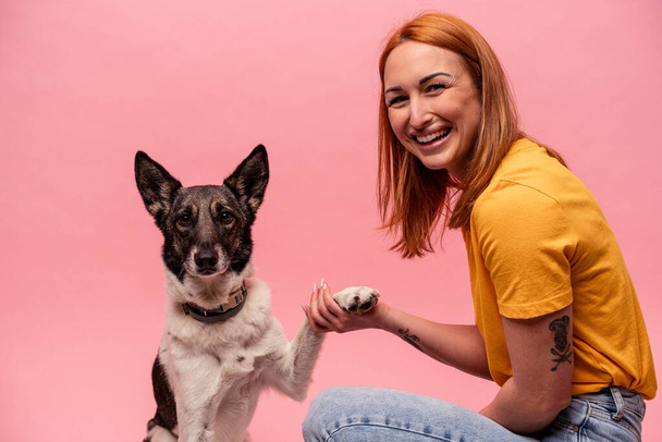 Joven mujer caucásica con su perro aislado sobre fondo rosa - Foto, Imagen