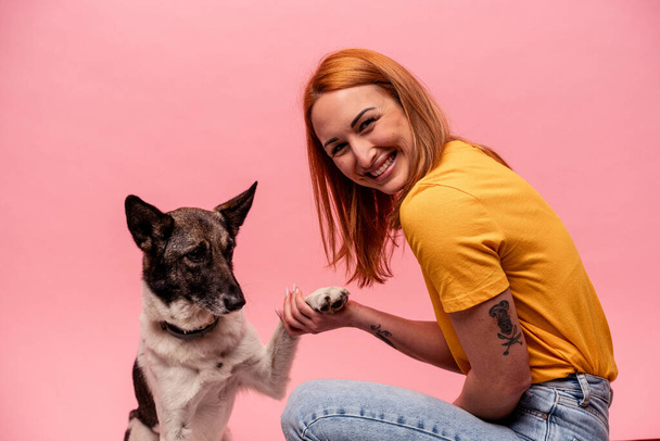 Junge kaukasische Frau mit Hund isoliert auf rosa Hintergrund - Foto, Bild