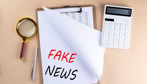 Clipboard with chart and text FAKE NEWS with magnifier ,calculator on a beige background - Photo, Image
