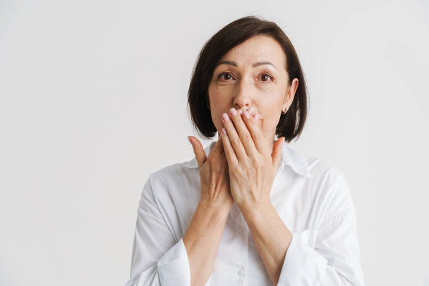 European mature woman looking aside while covering her mouth isolated over white wall - Photo, image