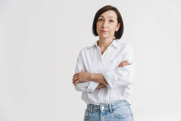 European mature woman looking at camera while posing with arms crossed isolated over white wall - Foto, Bild