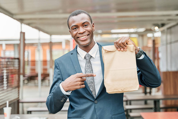 человек в костюме и галстук указывает на бумажный пакет с копировальным местом для текста или логотипа - Фото, изображение