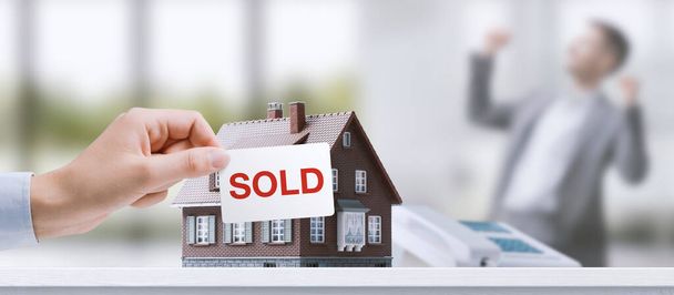 Real estate agent holding a sold sign in front of a model house, successful sale concept - Foto, immagini