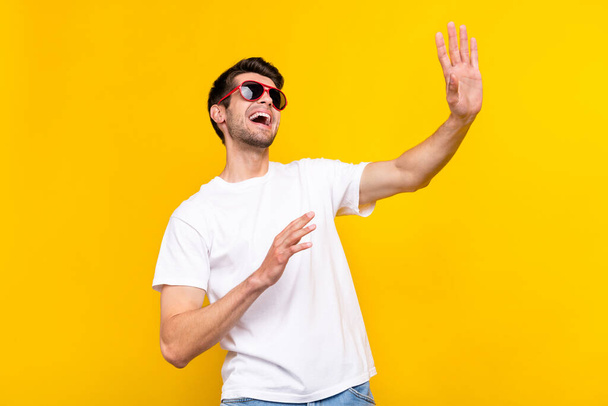 Photo of impressed millennial brunet guy dance wave wear glasses t-shirt isolated on yellow color background - Fotoğraf, Görsel