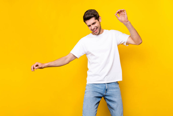 Photo of cute millennial brunet guy dance wear t-shirt jeans isolated on yellow color background - Foto, imagen