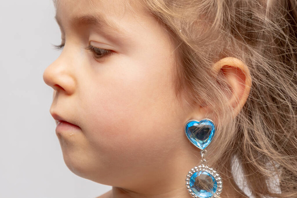 Una bambina in una corona e orecchini dimostra anelli giocattolo sulle dita, gioielli per bambini e gioielli costume. - Foto, immagini