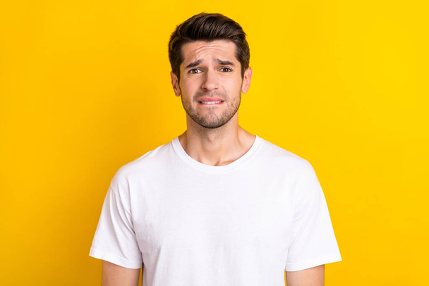 Photo of sorry worried nervous scared man bite lip look camera wear white t-shirt isolated yellow color background - Fotó, kép