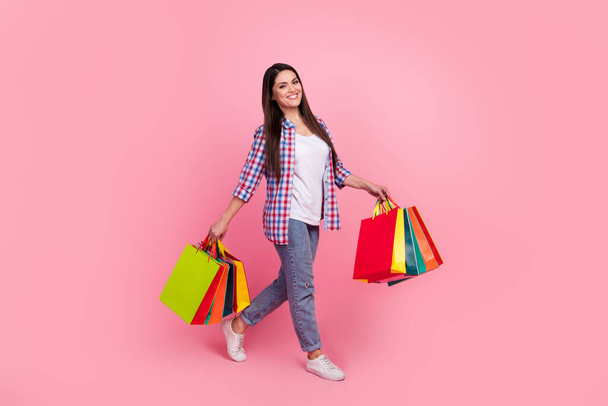 Full body photo of sweet mature brunette lady hold bags go wear shirt jeans footwear isolated on pink background - Fotoğraf, Görsel