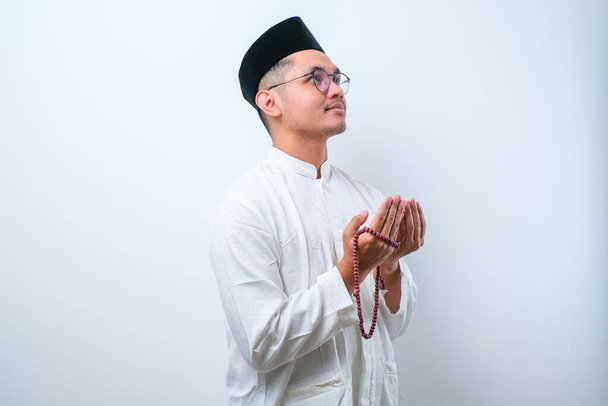 Мусульманин-азіат у муслімному одязі з намистинами для молитви, що аплодують Богу на білому тлі. - Фото, зображення