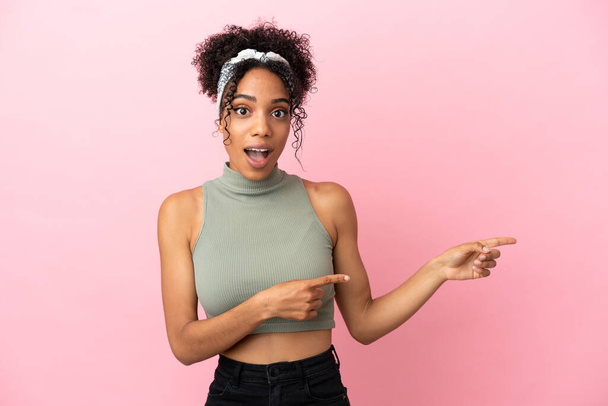 Young latin woman isolated on pink background surprised and pointing side - Фото, изображение