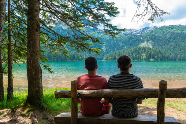 Toeristen op een houten bank bij Glacial Black Lake. Toeristische attractie van Durmitor National Park. Wandelpad cirkelt rond het meer, en is populaire bestemming voor recreatie en wandelen. Montenegro - Foto, afbeelding