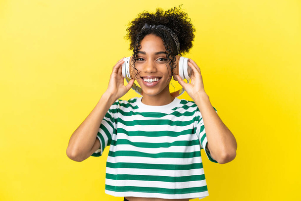 Sarı arka planda izole edilmiş genç Afrikalı Amerikalı kadın müzik dinliyor. - Fotoğraf, Görsel