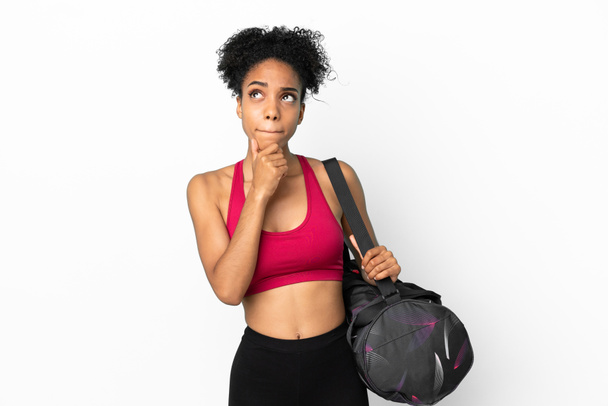 若いスポーツアフリカ系アメリカ人女性スポーツバッグと青の背景に隔離された疑問と思考を持っている - 写真・画像