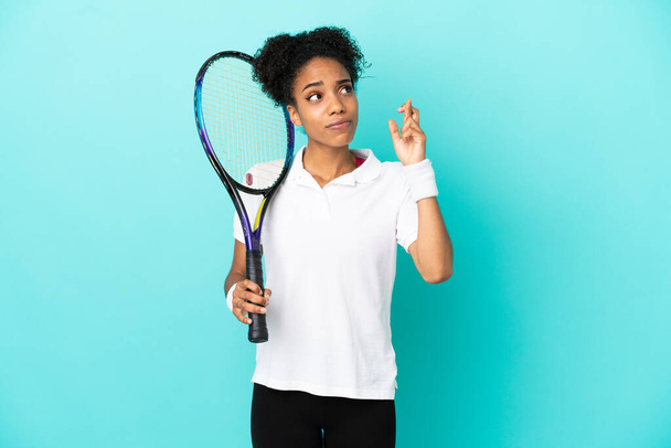 Young tennis player woman isolated on blue background with fingers crossing and wishing the best - Foto, imagen