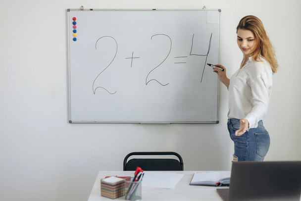 E-learning. Jeune enseignante debout dans la salle de classe devant un ordinateur portable et menant une leçon de mathématiques en ligne par chat vidéo. Le concept d'enseignement à distance. - Photo, image