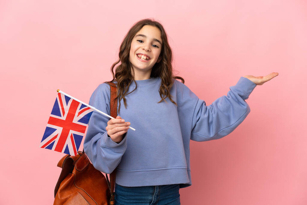 Menina segurando uma bandeira do Reino Unido isolado em fundo rosa estendendo as mãos para o lado para convidar para vir - Foto, Imagem