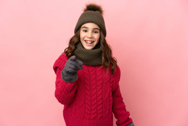 Little girl with winter hat isolated on pink background surprised and pointing front - Photo, image