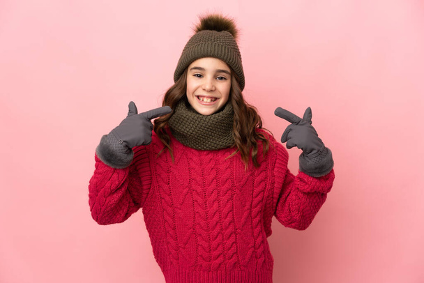 Menina com chapéu de inverno isolado no fundo rosa dando um gesto polegares para cima - Foto, Imagem