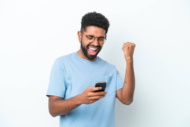 Mladý brazilský muž izolované na bílém pozadí s telefonem ve vítězné pozici - Fotografie, Obrázek
