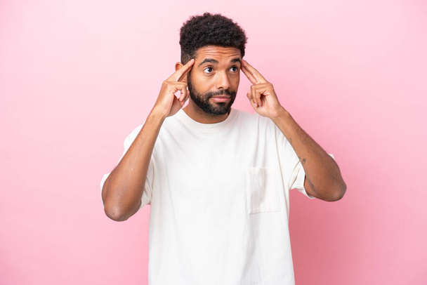 Young Brazilian man isolated on pink background having doubts and thinking - Photo, Image