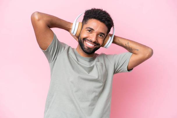 Young Brazilian man isolated on pink background listening music - Zdjęcie, obraz