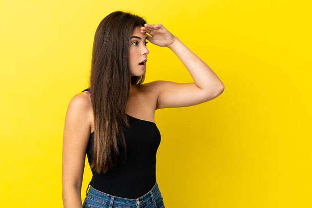 Young Brazilian woman isolated on yellow background with surprise expression while looking side - Foto, immagini
