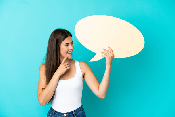 Young Brazilian woman isolated on blue background holding an empty speech bubble and pointing it - Фото, зображення