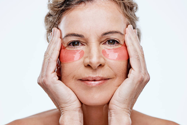Taking care of your skin will keep it younger for longer. Shot of a mature woman wearing under-eye gel patches while posing against a white background. - Fotografie, Obrázek