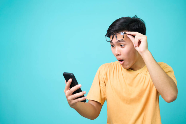 Jeune homme asiatique avec expression faciale surprise tenir smartphone dans ses mains. - Photo, image
