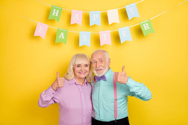 Portrait of two attractive cheerful grey-haired spouses hugging showing thumbup easter isolated over bright yellow color background - Photo, Image